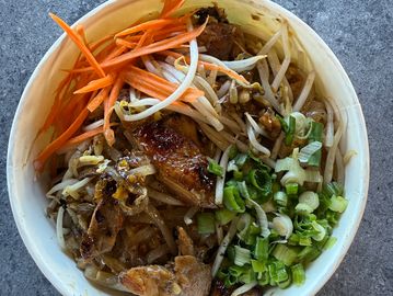 A bowl of grilled chicken with bean sprouts, shredded carrots, and chopped green onions.