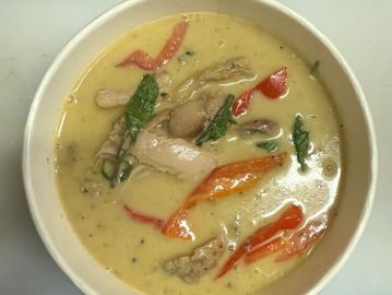 A bowl of creamy Thai green curry with chicken and vegetables.
