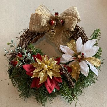 A Christmas wreath featuring red and white flowers, gold ribbon and greenery.