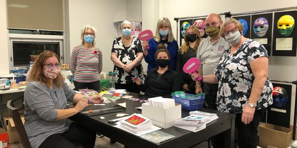 BIAWW staff and brain injury survivors pose around a table of art supplies.