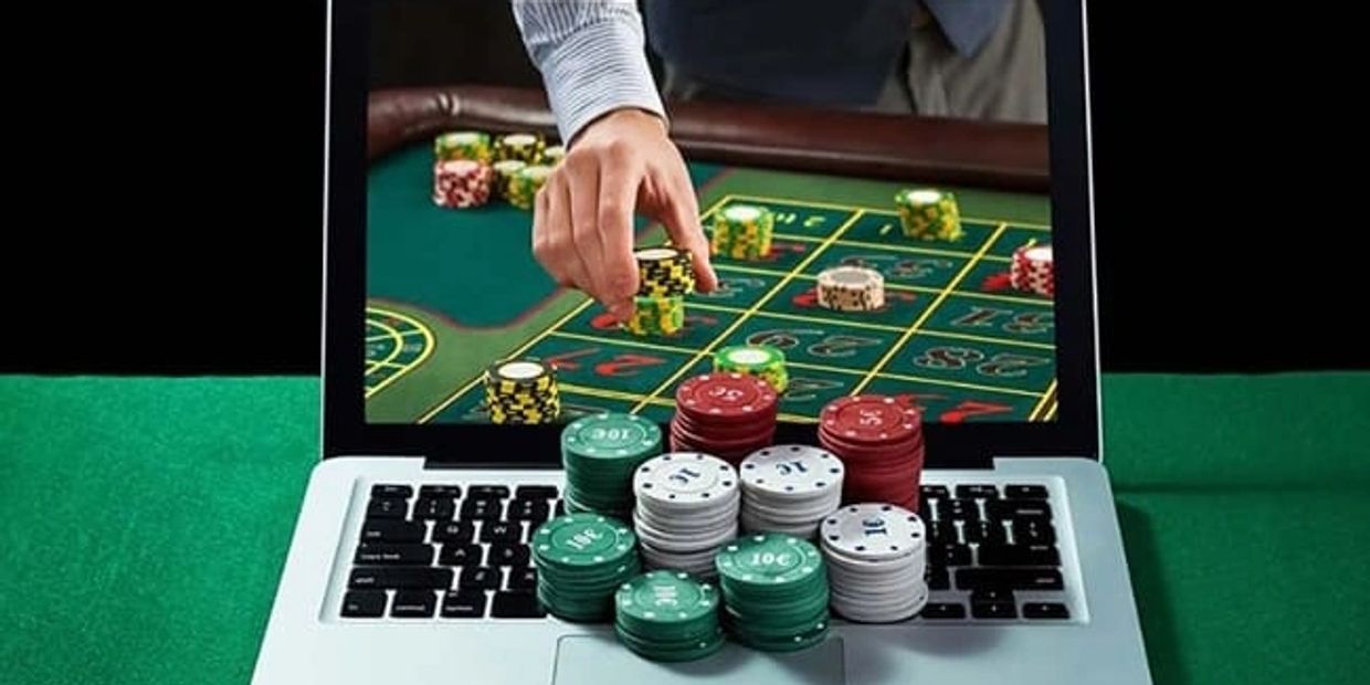 Hand placing chips on a virtual roulette table shown on a laptop.