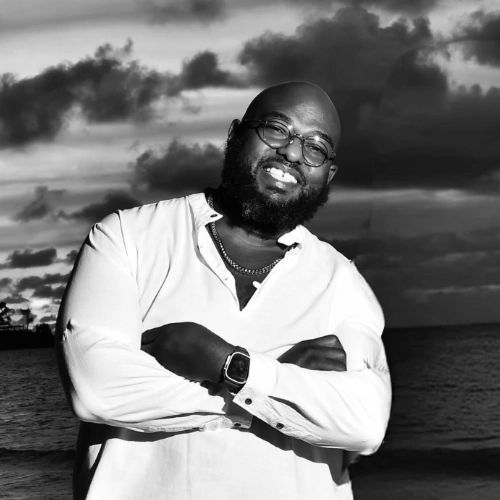 Smiling man in white shirt by the ocean at sunset.