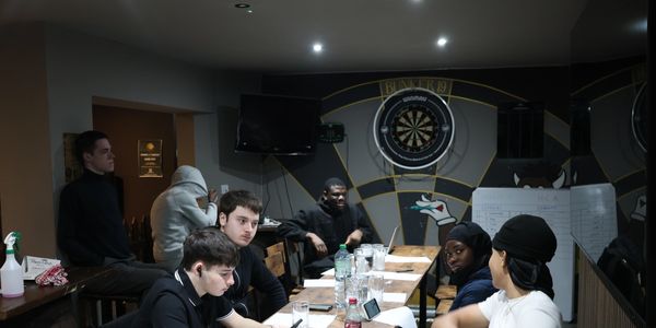 Young people gathered around a table in a casual meeting room with dartboard.