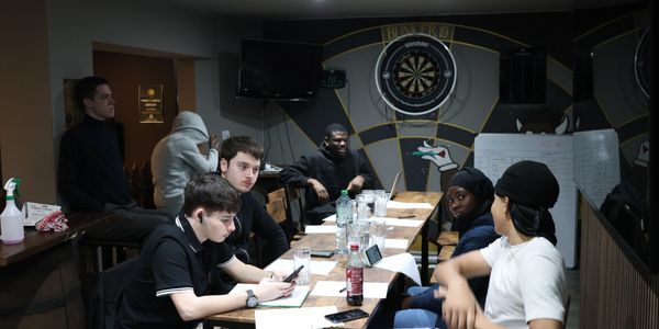 Young people gathered around a table in a casual meeting room with dartboard.