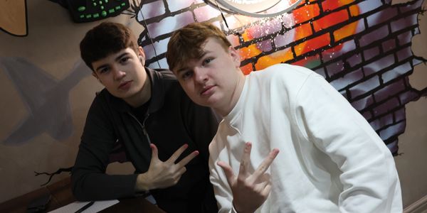 Two young men posing with hand signs in a room with graffiti wall art.