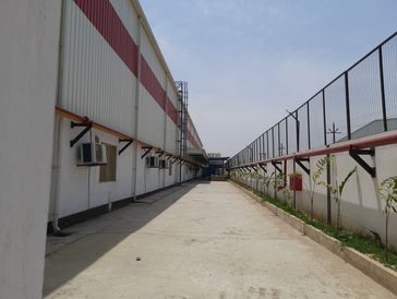 Empty industrial walkway between metal buildings and fences.