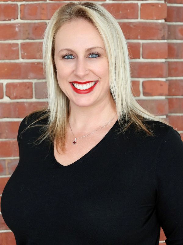 Smiling woman with blonde hair and red lipstick in front of a brick wall.