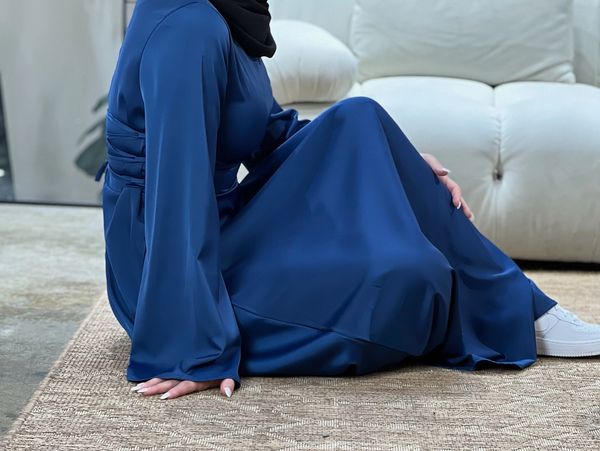 Person sitting on a beige patterned rug wearing a blue dress and white sneakers.