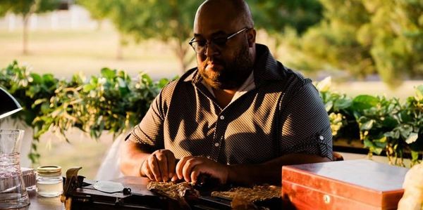 Man rolling a cigar at a wooden table outdoors.