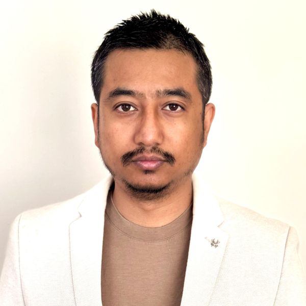 Portrait of a man in a beige blazer and brown shirt against a plain background.