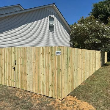New wooden privacy fence around a backyard under clear blue sky.