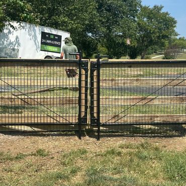 Newly installed wooden and wire fence gate with a man and a trailer in the background.