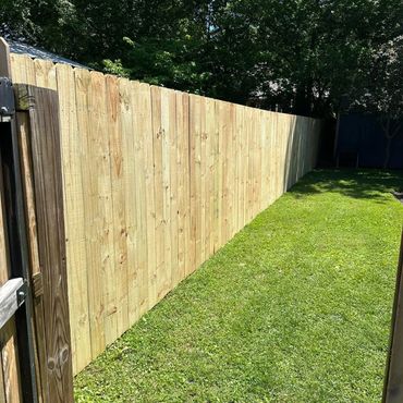 A newly installed wooden fence bordering a green backyard lawn on a sunny day.