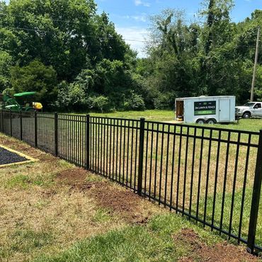 Black metal fence dividing a grassy area with trees in the background.