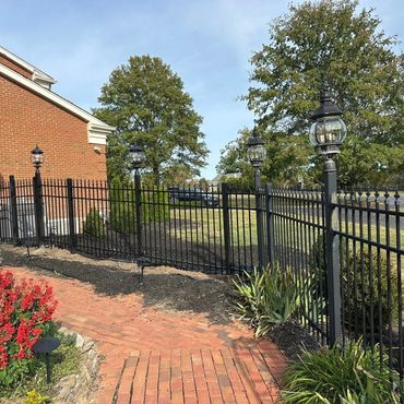 Black iron fence with lanterns surrounding a brick house and garden.