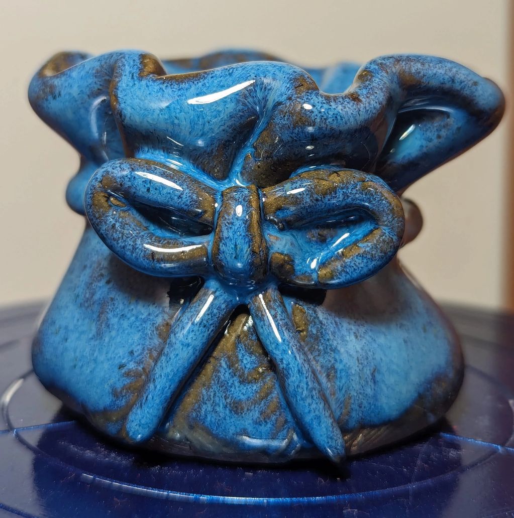 Small medium blue pinch pot with fluted rim and added clay bow.