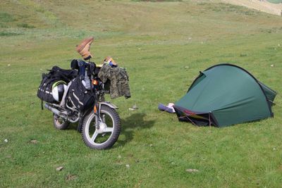 Motorcycle camping setup with a green tent on grass.