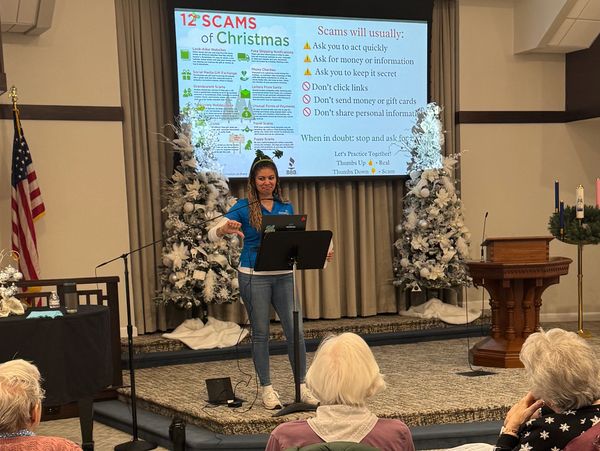 Presenter talks about 12 Christmas scams to an audience in a decorated room.
