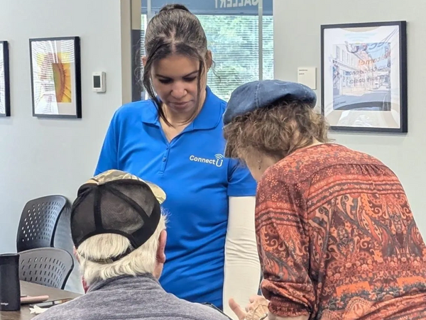 A young woman assists two elderly individuals in an indoor setting.