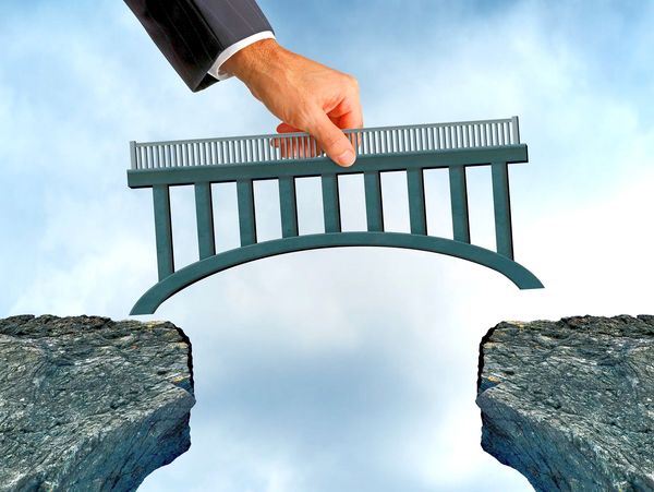Hand placing a bridge model to connect two rocky cliffs.