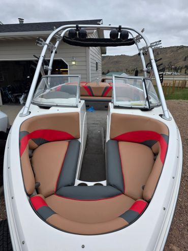 Front view of a modern boat with cushioned seating in beige, red, and black colors.
