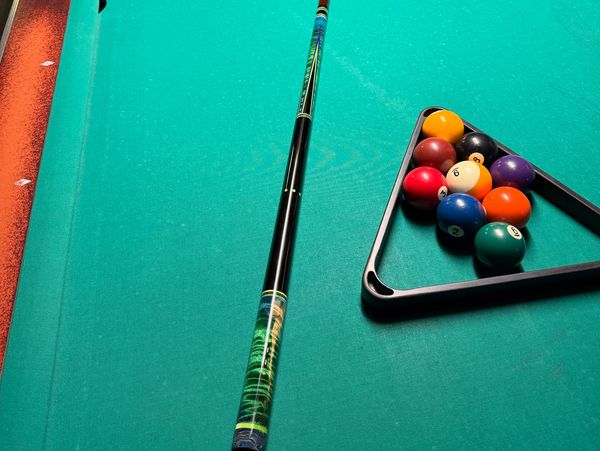 A pool cue and racked billiard balls on a green pool table.
