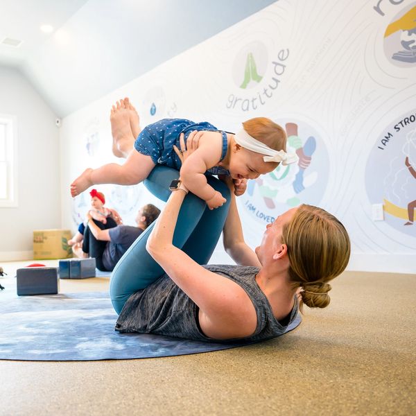 Mother holding her baby in boat pose during a postnatal & baby yoga class in Bucks County, PA