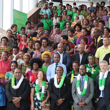 A large group of people posing on stairs, many wearing colorful traditional attire and green leis.