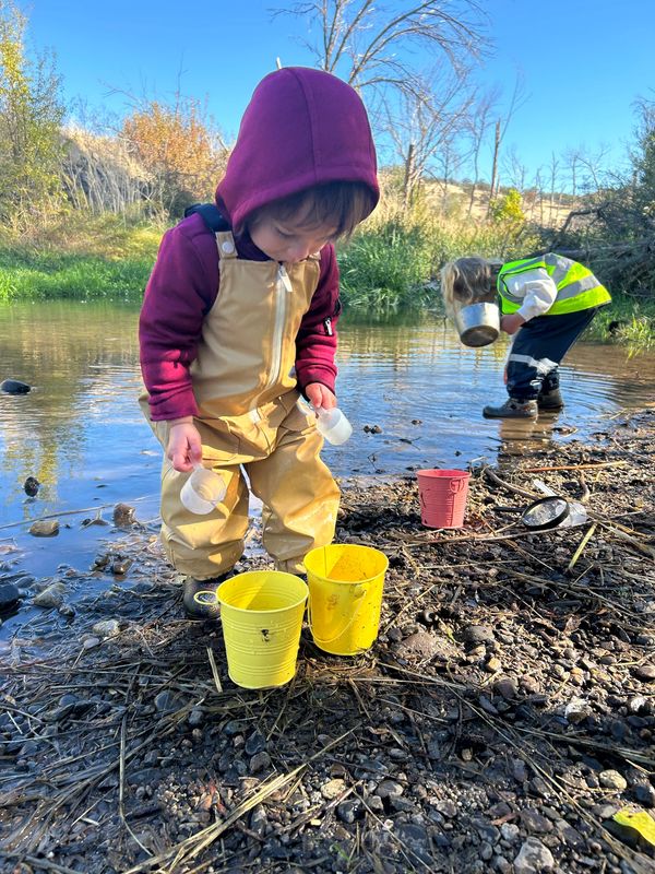 toddler and preschooler playing in creek with buckets.