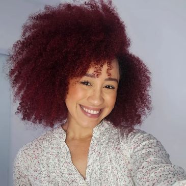 Smiling woman with voluminous curly red hair in a floral blouse.