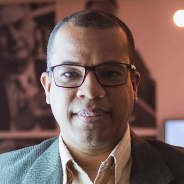 Man wearing glasses and a blazer smiling indoors.