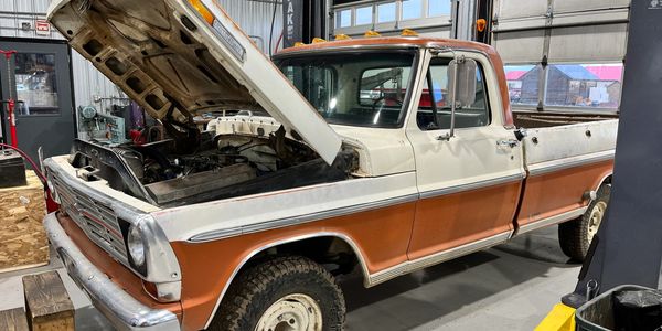 Vintage two-tone pickup truck with open hood in workshop.