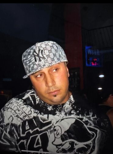 Man wearing a patterned cap and graphic hoodie in a dimly lit room.