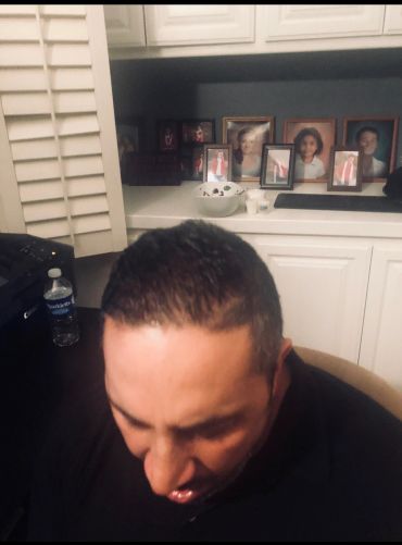 Man with short hair looking down in a room with family photos.