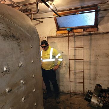 Worker inspecting large metal tank in industrial basement.