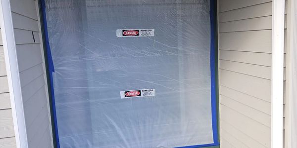 A door sealed with plastic sheeting and asbestos danger signs.