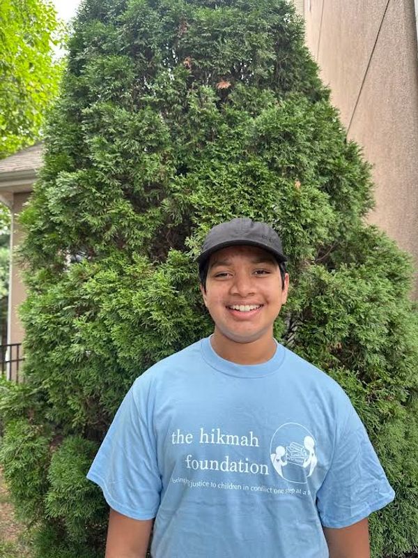 Smiling young man in a blue 'the hikmah foundation' t-shirt.