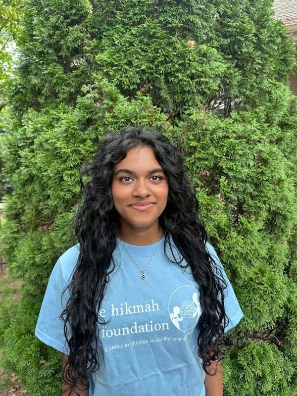 Young woman with long curly hair in a blue t-shirt stands outdoors.