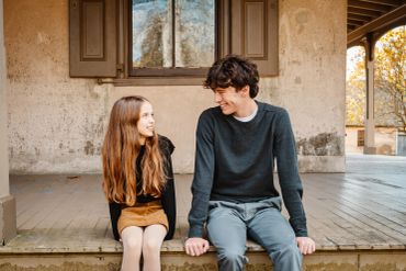 A young girl and a young man sit together on wooden steps, smiling at each other.