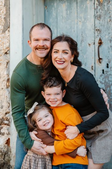 A happy family of four posing together outdoors.