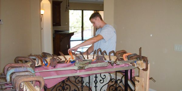 Man working on a large woodworking project with numerous clamps indoors.