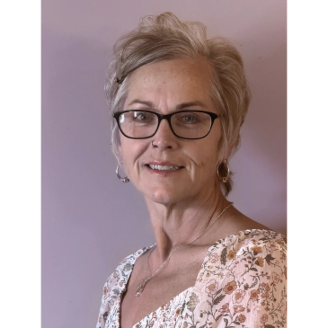 Headshot of therapist Annette E. Wheeler smiling, wearing glasses and a floral print shirt.