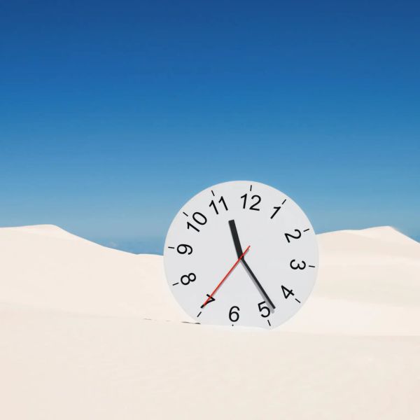 Clock partially buried in white sand dunes under a clear blue sky.