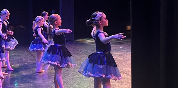 Young ballerinas in blue tutus practicing on stage.