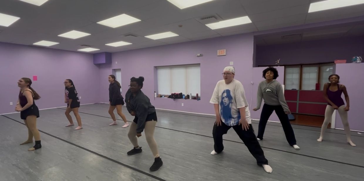 A diverse group of dancers practicing in a purple-walled studio.