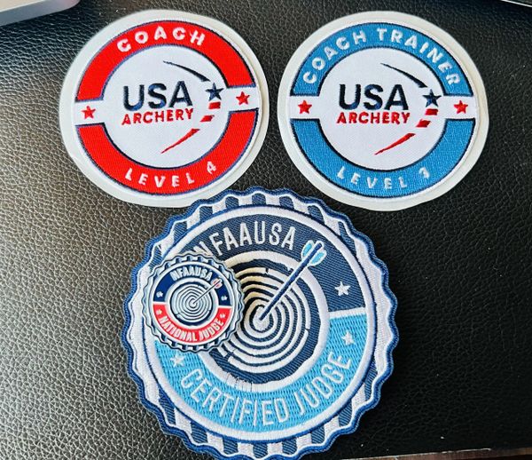Three USA Archery and NFAA certified coach and judge patches on black surface.