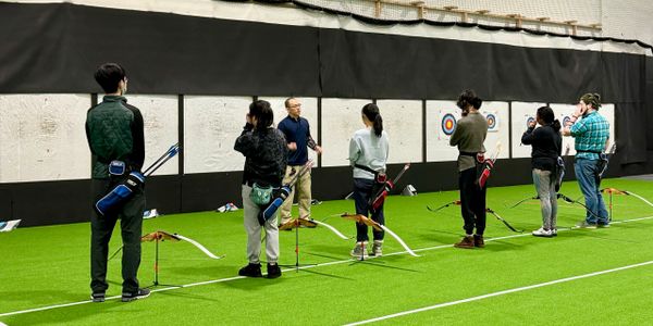 A group taking archery lessons indoors with instructor guidance.