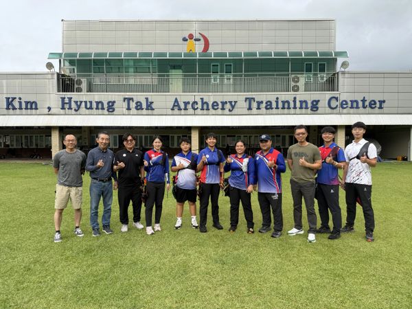 Group photo of archery team members standing in front of Kim Hyung Tak Archery Training Center.