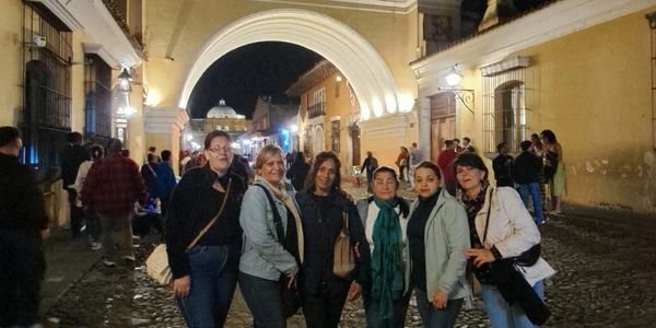 Group of six women posing at night under a lit archway in a historic street.