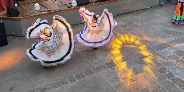 Two dancers in traditional dresses twirling with vibrant patterns under warm lighting.